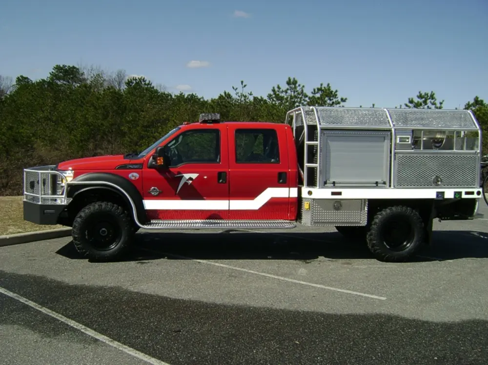 Exterior view of small fire truck showing cab, body compartments, and wheel/tire area.