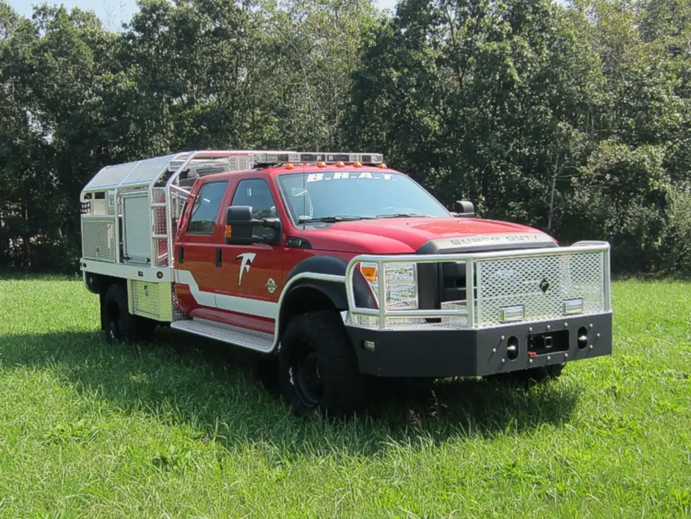 Exterior view of small fire truck showing cab, body compartments, and wheel/tire area.