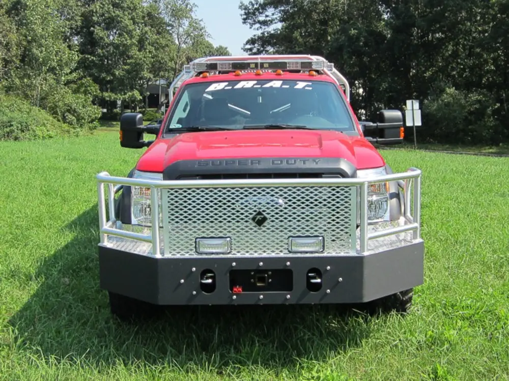Exterior view of small fire truck showing cab, body compartments, and wheel/tire area.