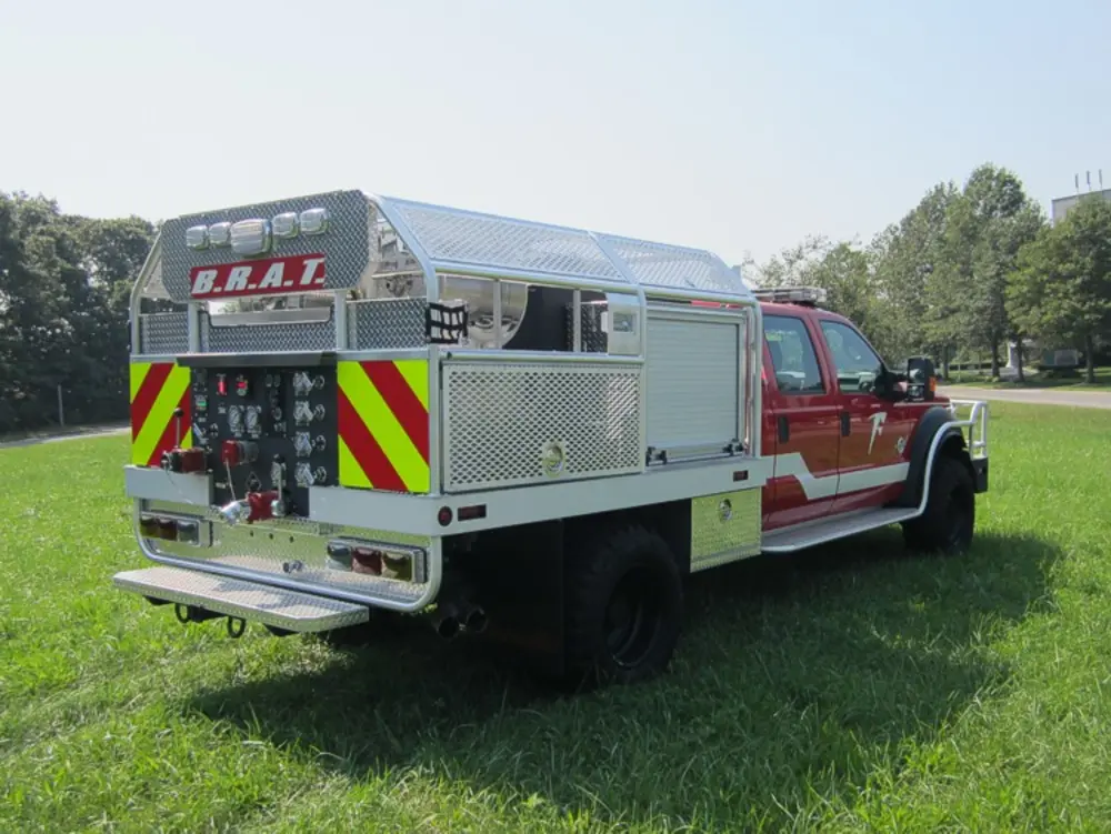 Exterior view of small fire truck showing cab, body compartments, and wheel/tire area.