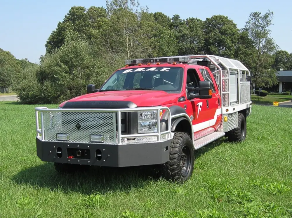 Exterior view of small fire truck showing cab, body compartments, and wheel/tire area.