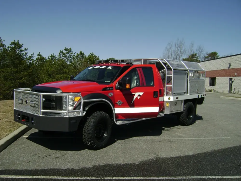 Exterior view of small fire truck showing cab, body compartments, and wheel/tire area.