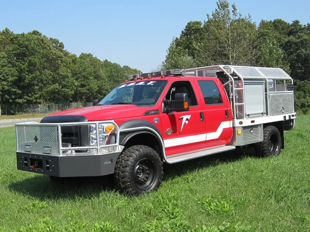 Exterior view of small fire truck showing cab, body compartments, and wheel/tire area.