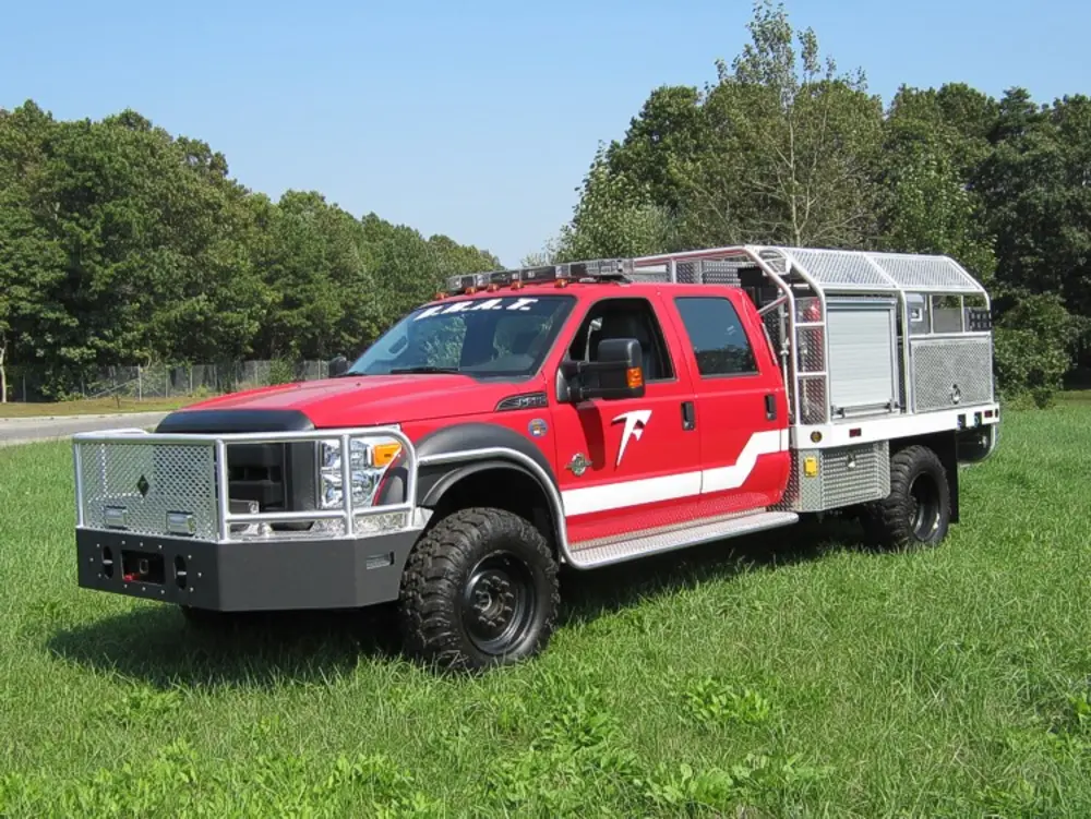 Exterior view of small fire truck showing cab, body compartments, and wheel/tire area.