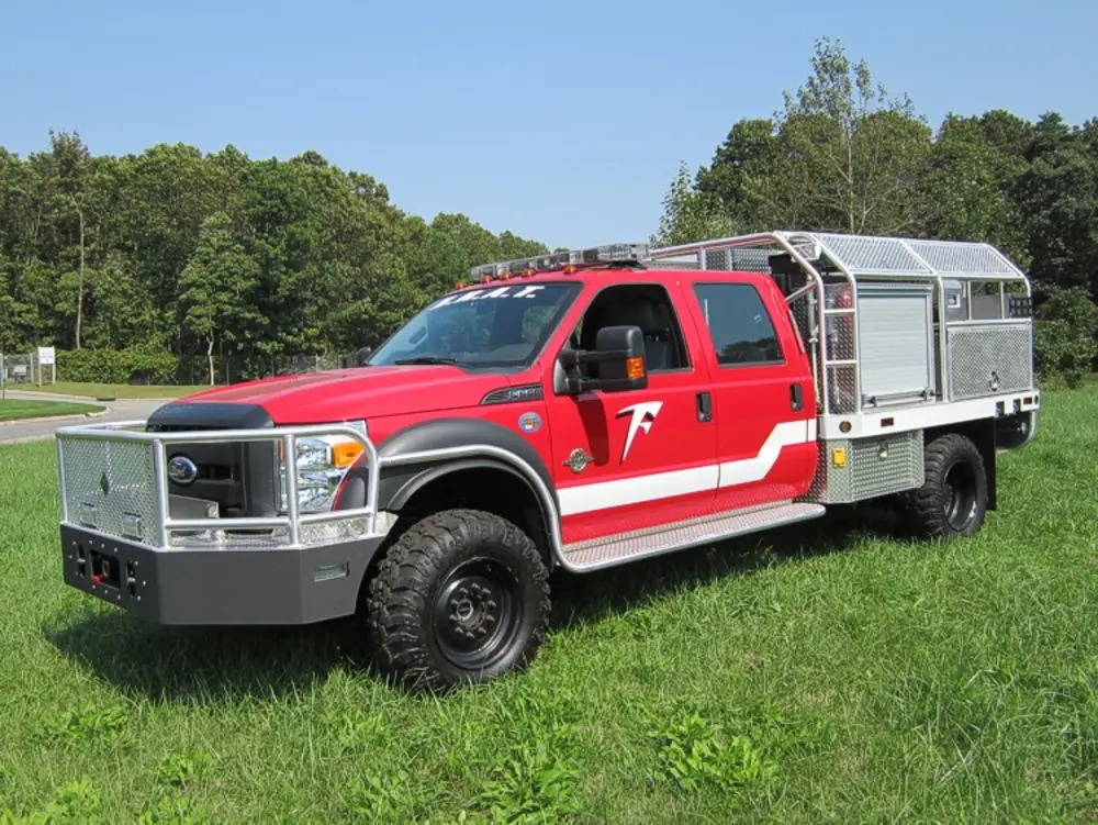 Exterior view of small fire truck showing cab, body compartments, and wheel/tire area.