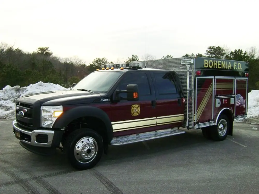 Exterior view of small fire truck showing cab, body compartments, and wheel/tire area.
