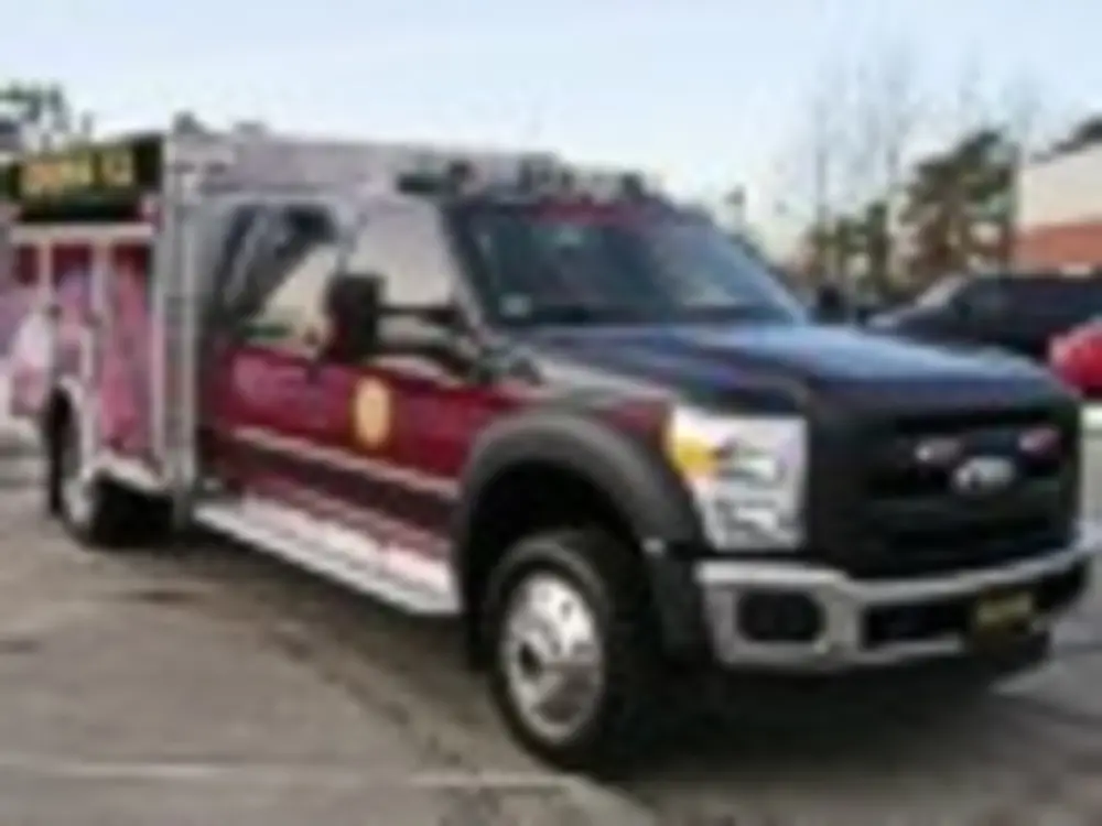 Exterior view of small fire truck showing cab, body compartments, and wheel/tire area.