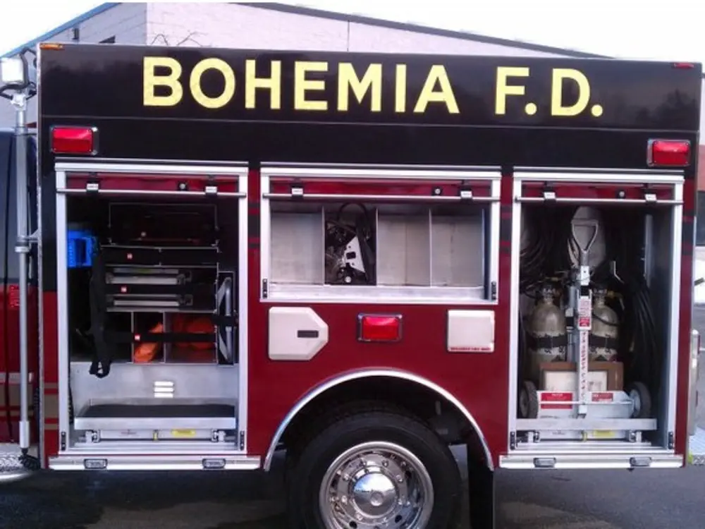 Exterior view of small fire truck showing cab, body compartments, and wheel/tire area.