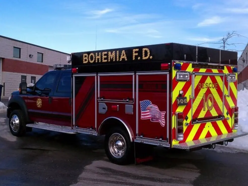 Exterior view of small fire truck showing cab, body compartments, and wheel/tire area.