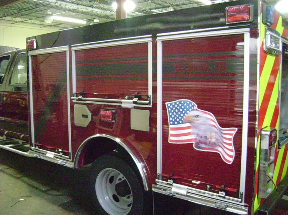 Exterior view of small fire truck showing cab, body compartments, and wheel/tire area.
