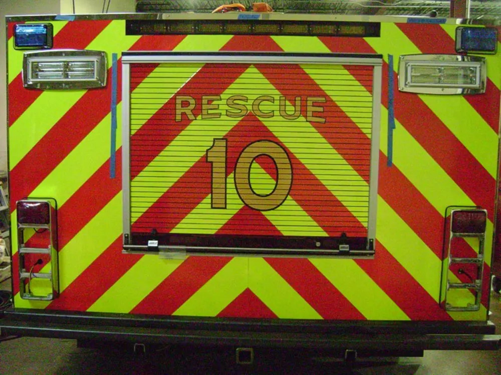 Exterior view of small fire truck showing cab, body compartments, and wheel/tire area.