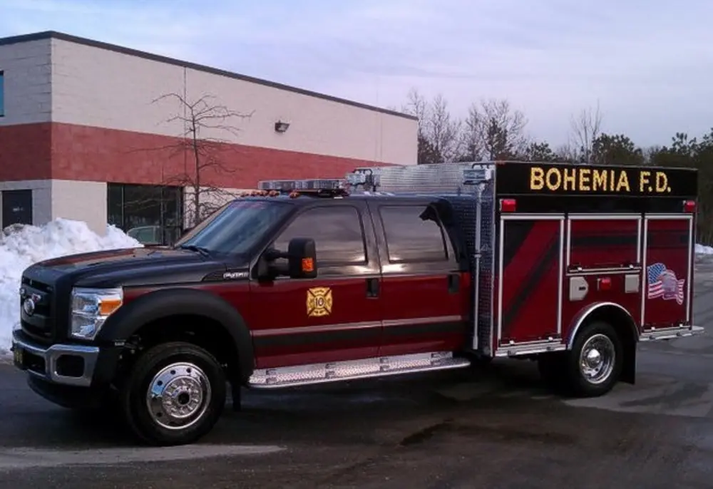Exterior view of small fire truck showing cab, body compartments, and wheel/tire area.