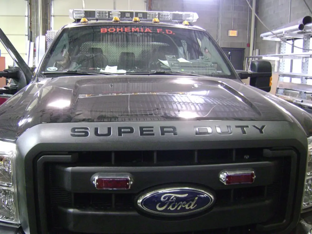 Exterior view of small fire truck showing cab, body compartments, and wheel/tire area.