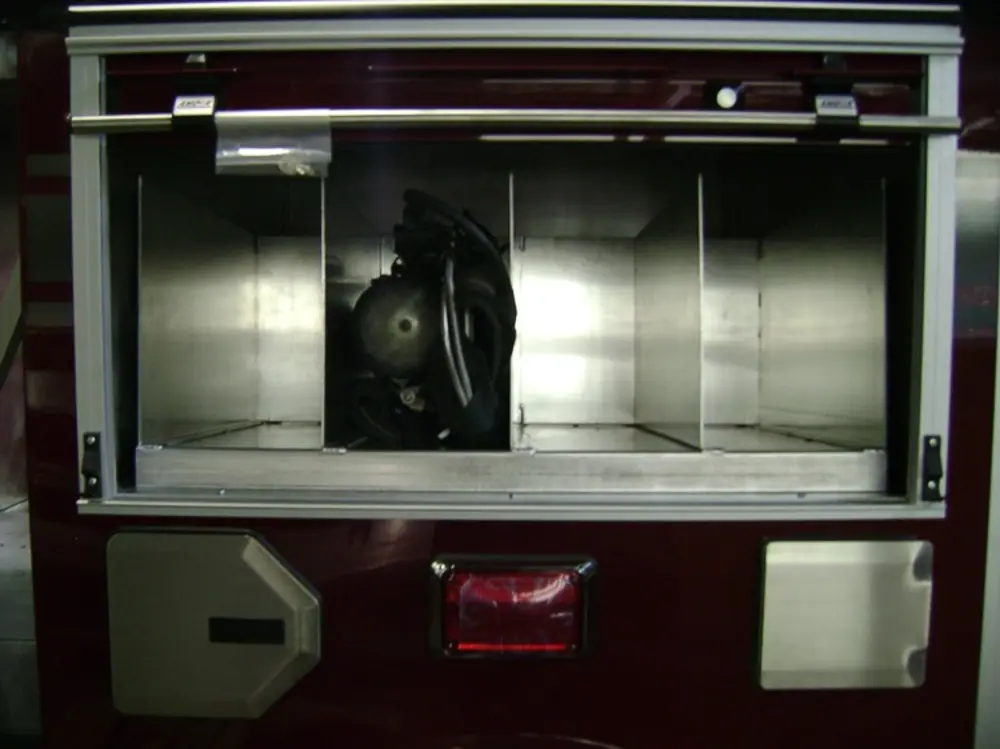 Exterior view of small fire truck showing cab, body compartments, and wheel/tire area.