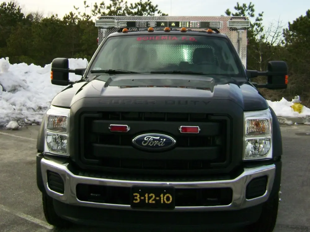Exterior view of small fire truck showing cab, body compartments, and wheel/tire area.