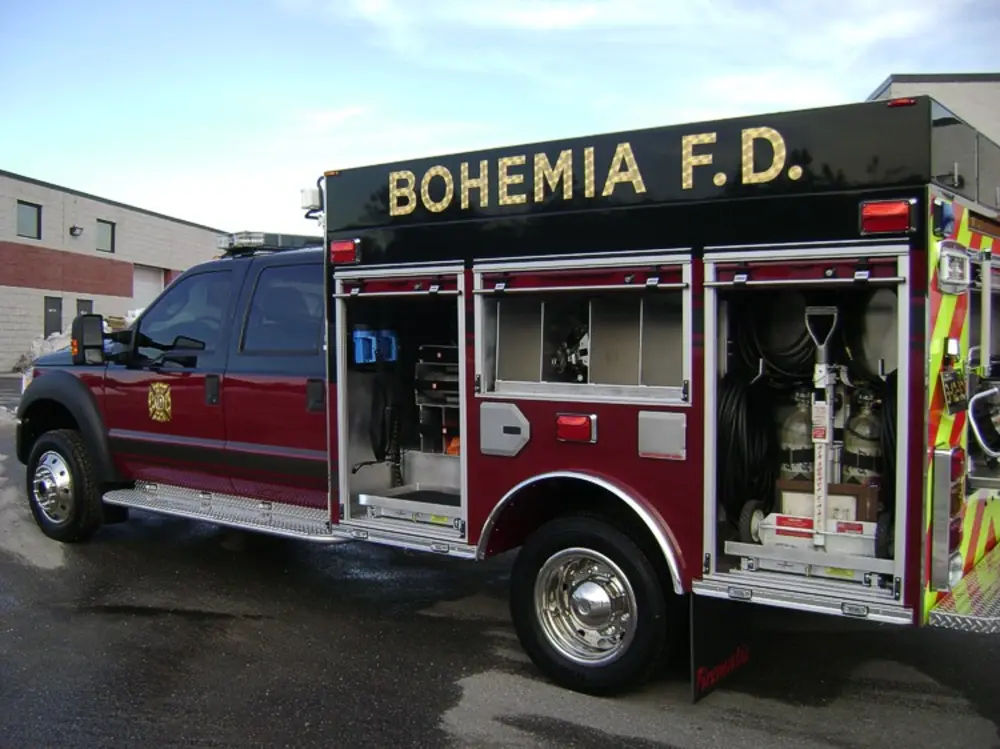 Exterior view of small fire truck showing cab, body compartments, and wheel/tire area.