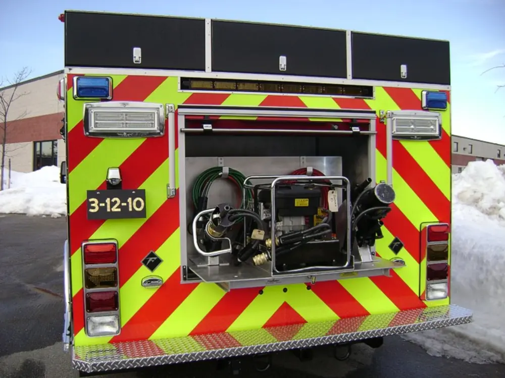 Exterior view of small fire truck showing cab, body compartments, and wheel/tire area.