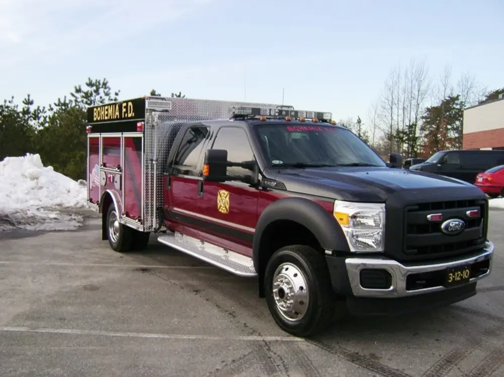 Exterior view of small fire truck showing cab, body compartments, and wheel/tire area.