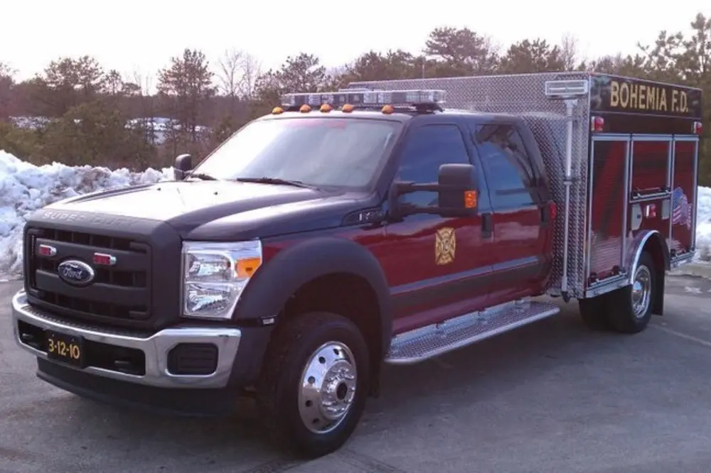 Exterior view of small fire truck showing cab, body compartments, and wheel/tire area.