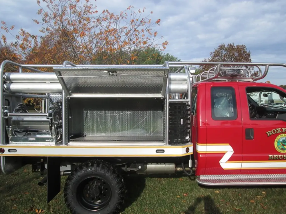 Exterior view of small fire truck showing cab, body compartments, and wheel/tire area.