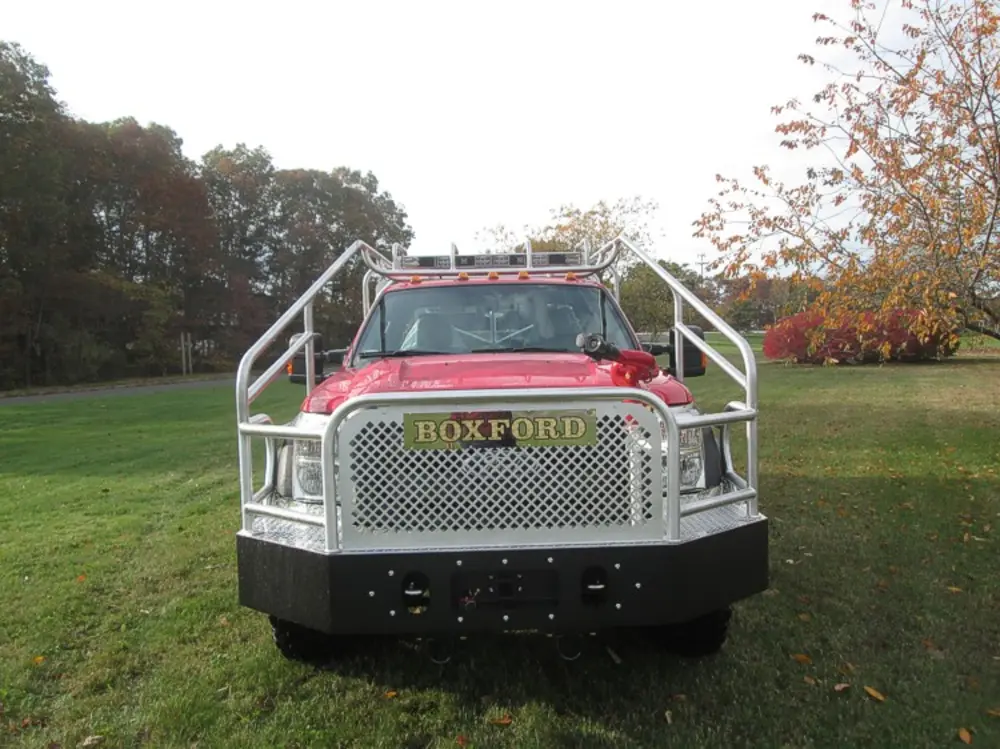 Exterior view of small fire truck showing cab, body compartments, and wheel/tire area.