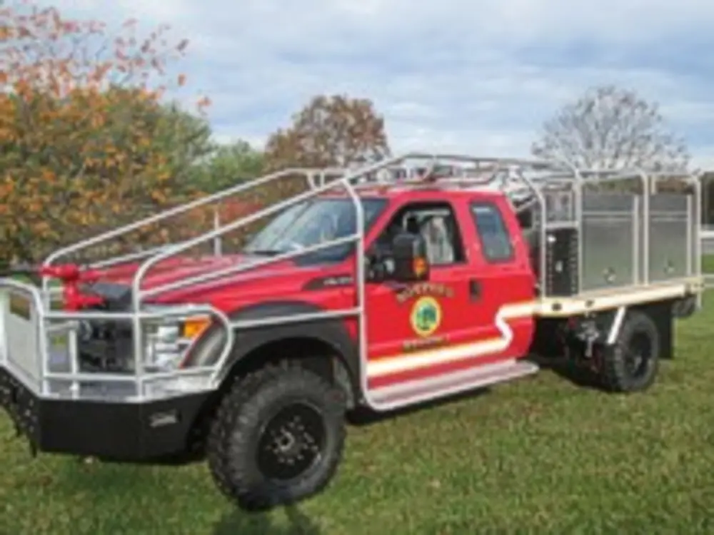 Exterior view of small fire truck showing cab, body compartments, and wheel/tire area.
