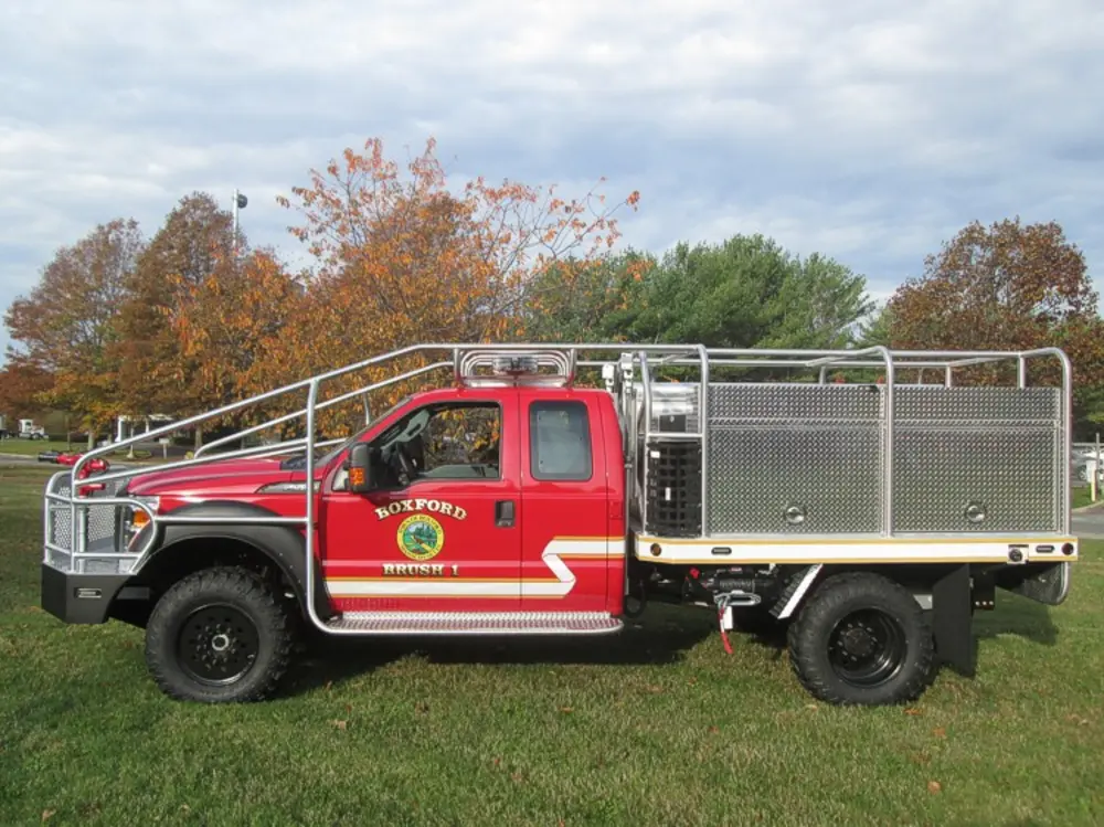 Exterior view of small fire truck showing cab, body compartments, and wheel/tire area.