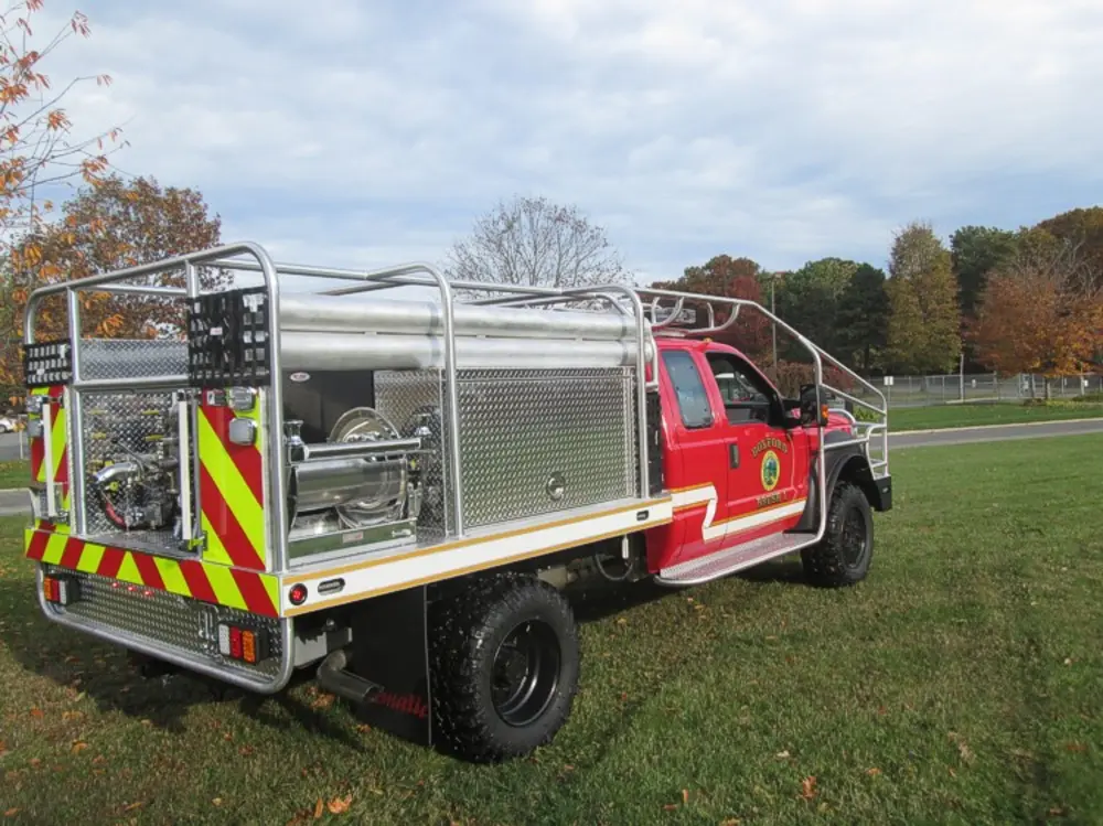 Exterior view of small fire truck showing cab, body compartments, and wheel/tire area.