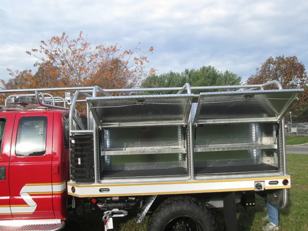 Exterior view of small fire truck showing cab, body compartments, and wheel/tire area.
