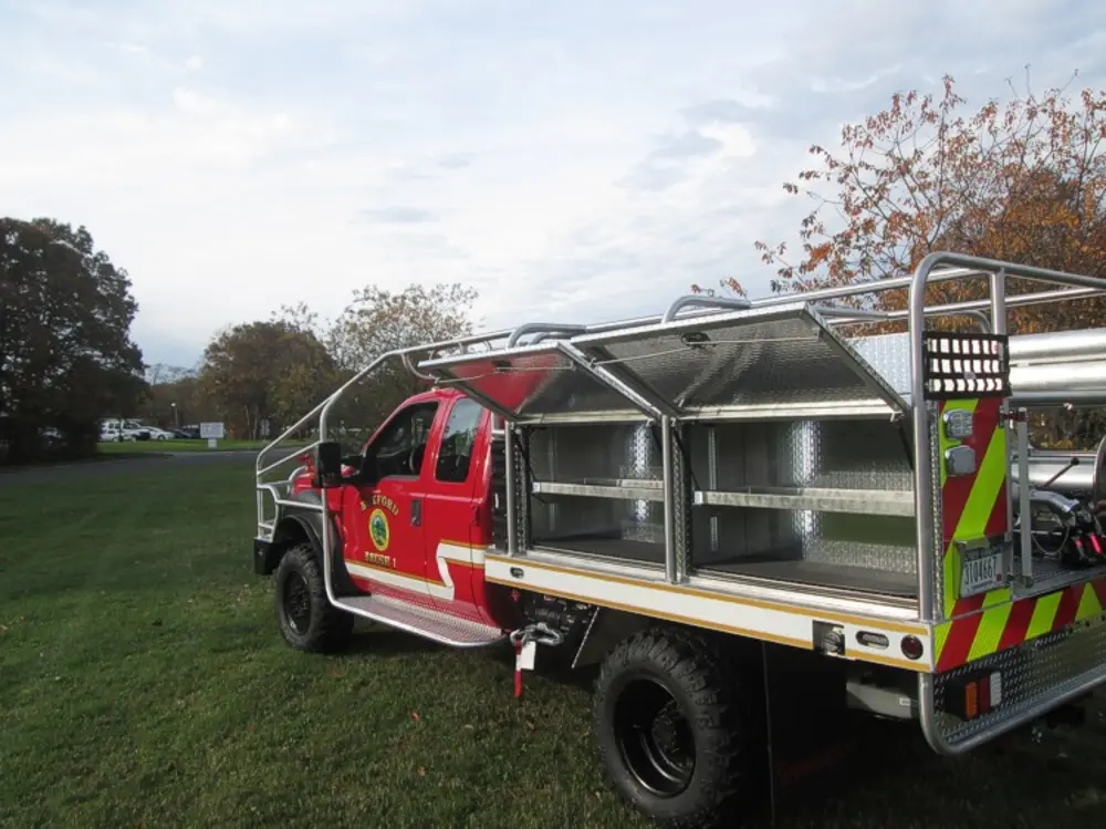 Exterior view of small fire truck showing cab, body compartments, and wheel/tire area.