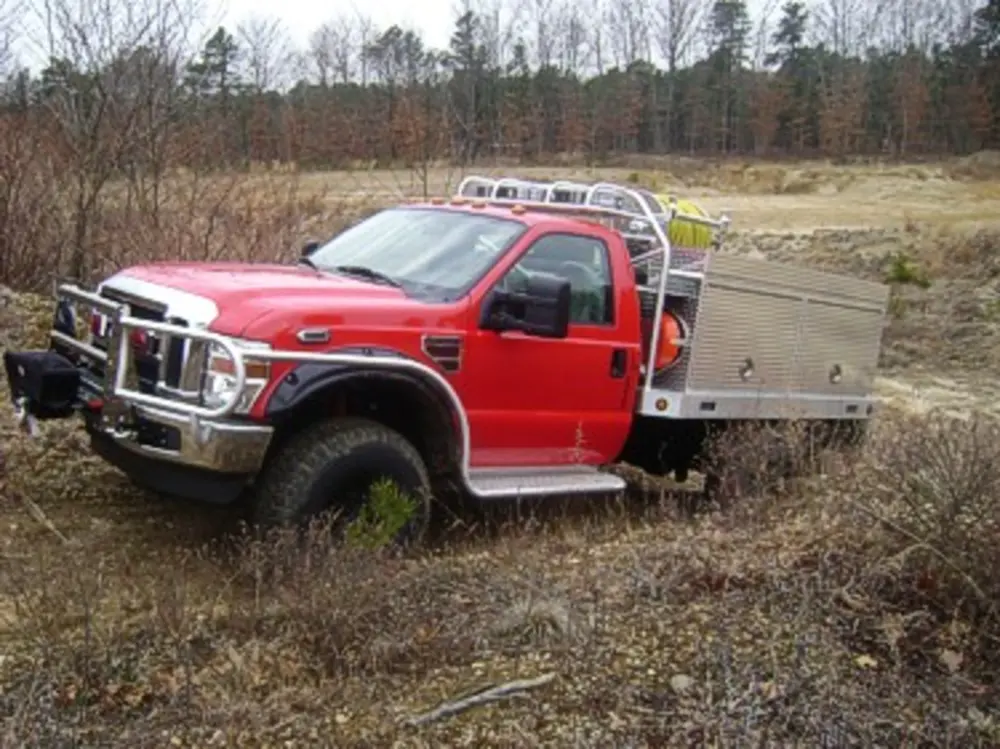 Exterior view of small fire truck showing cab, body compartments, and wheel/tire area.