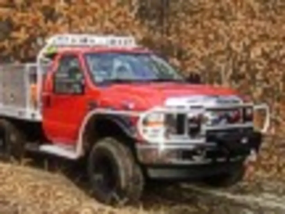 Exterior view of small fire truck showing cab, body compartments, and wheel/tire area.