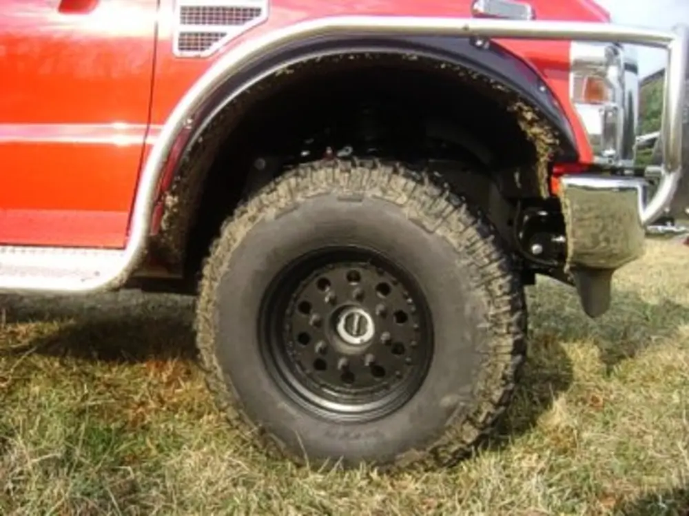 Exterior view of small fire truck showing cab, body compartments, and wheel/tire area.