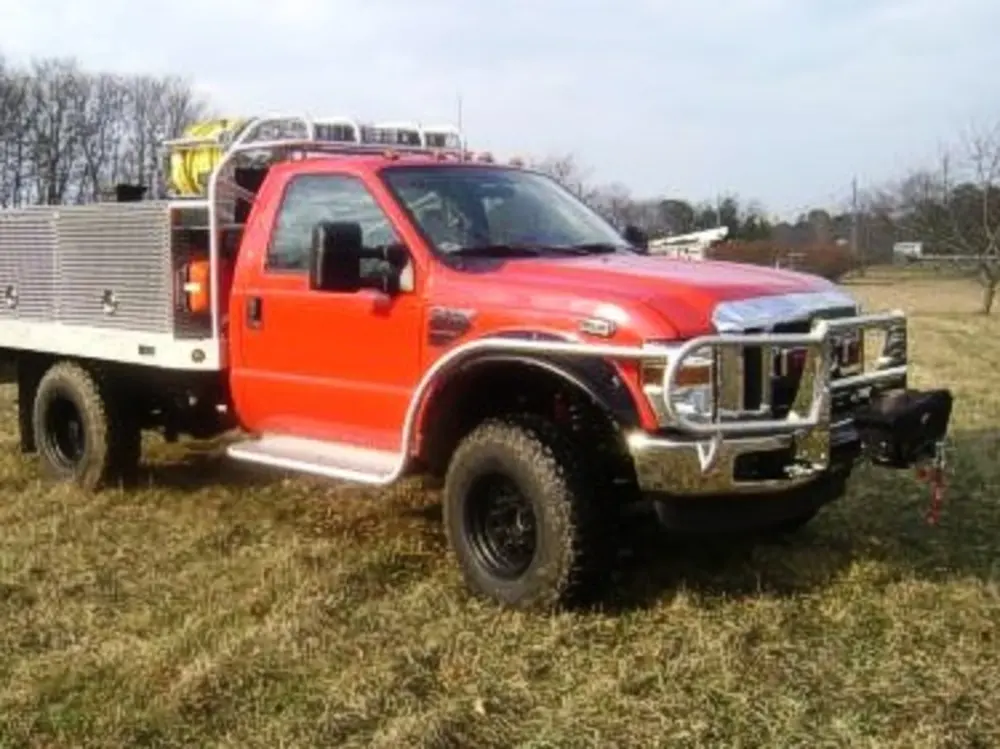 Exterior view of small fire truck showing cab, body compartments, and wheel/tire area.