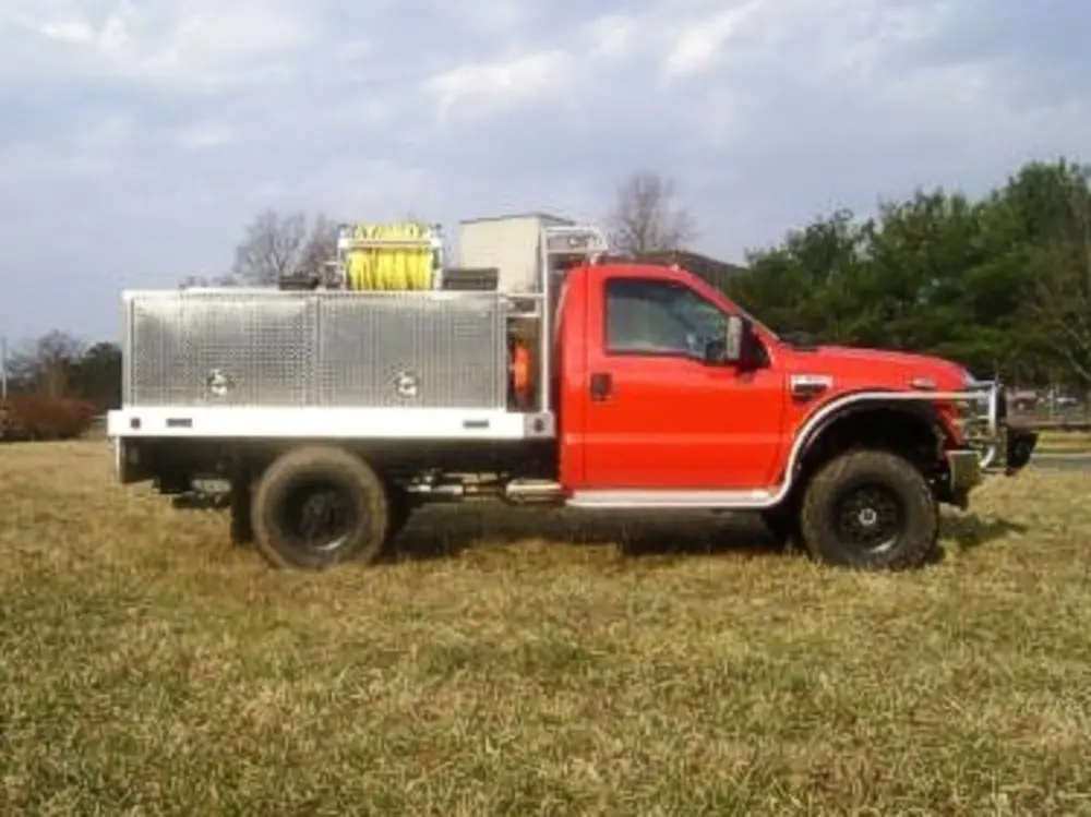 Exterior view of small fire truck showing cab, body compartments, and wheel/tire area.