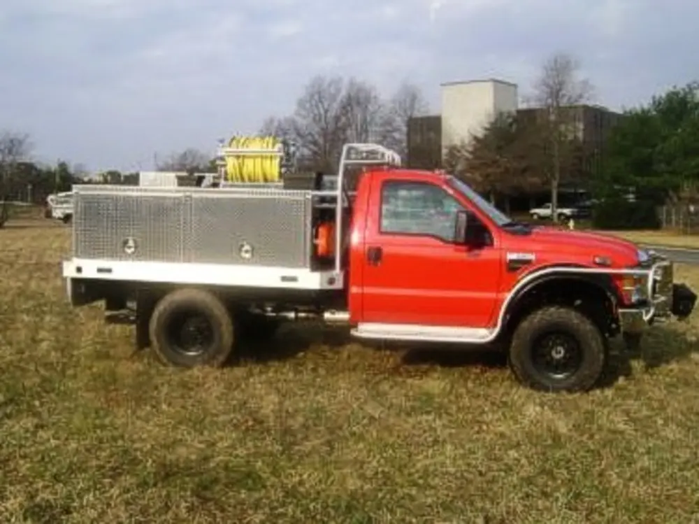 Exterior view of small fire truck showing cab, body compartments, and wheel/tire area.