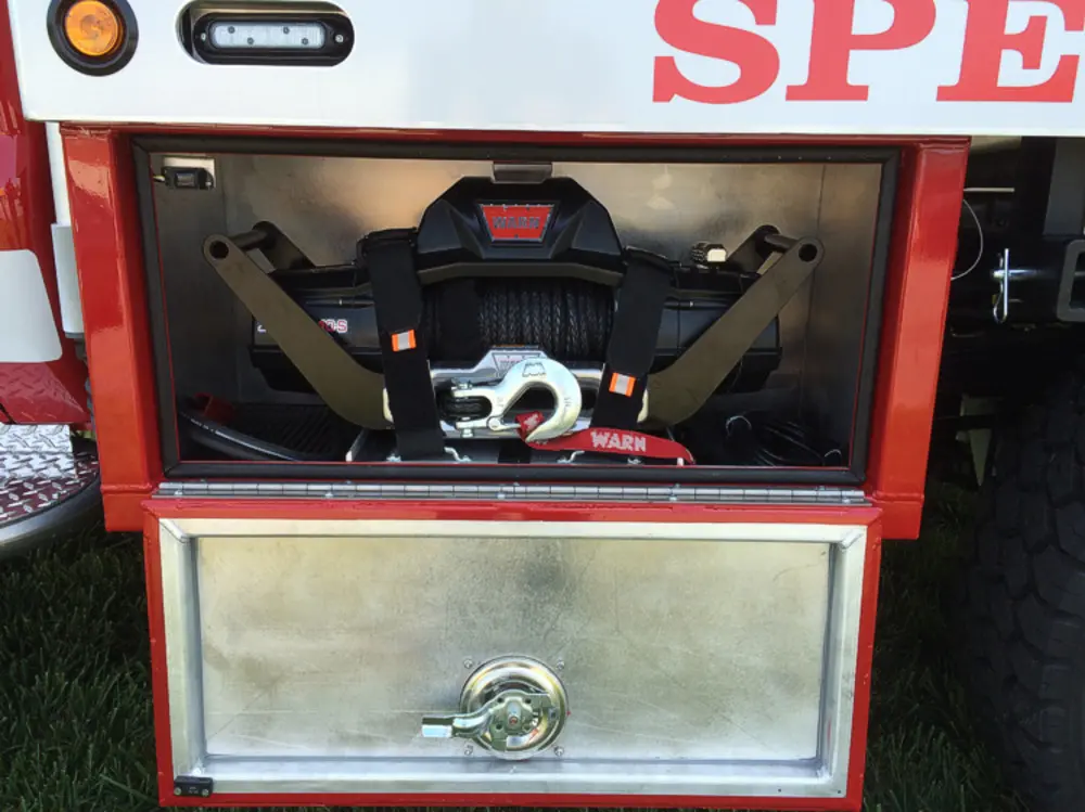 Exterior view of small fire truck showing cab, body compartments, and wheel/tire area.