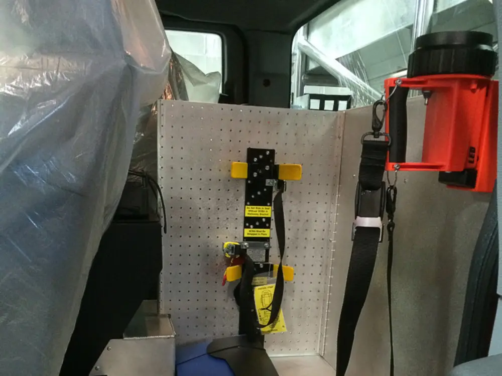 Exterior view of small fire truck showing cab, body compartments, and wheel/tire area.