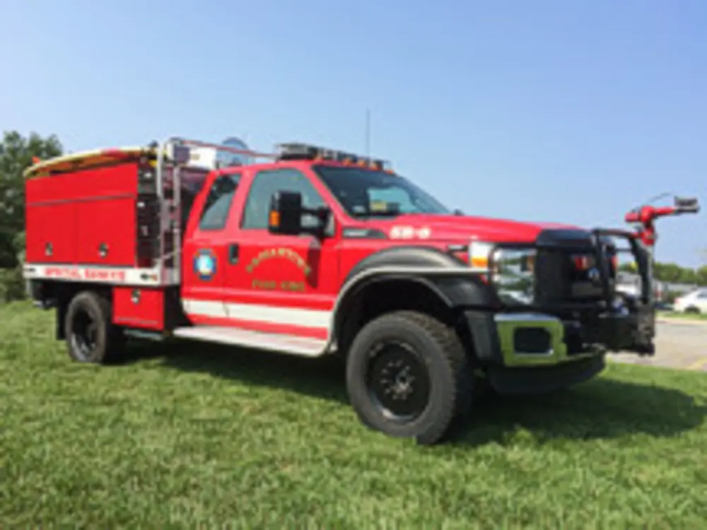 Exterior view of small fire truck showing cab, body compartments, and wheel/tire area.