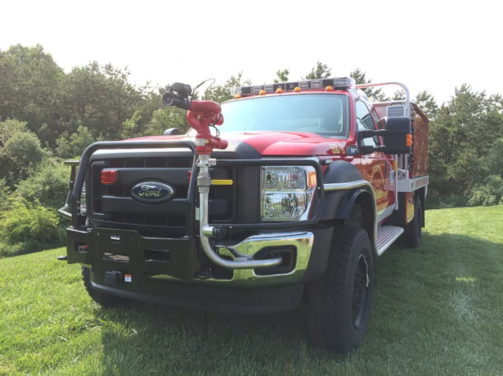 Exterior view of small fire truck showing cab, body compartments, and wheel/tire area.