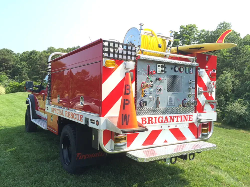Exterior view of small fire truck showing cab, body compartments, and wheel/tire area.