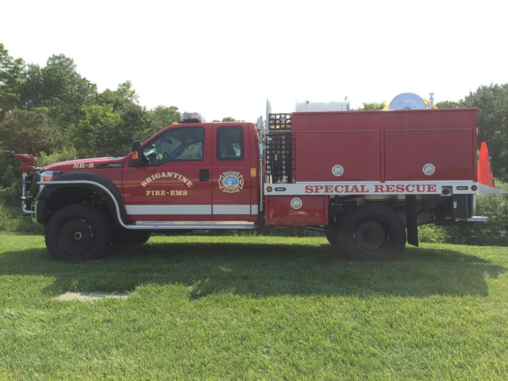 Exterior view of small fire truck showing cab, body compartments, and wheel/tire area.