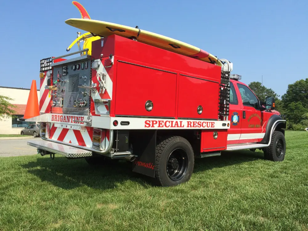 Exterior view of small fire truck showing cab, body compartments, and wheel/tire area.