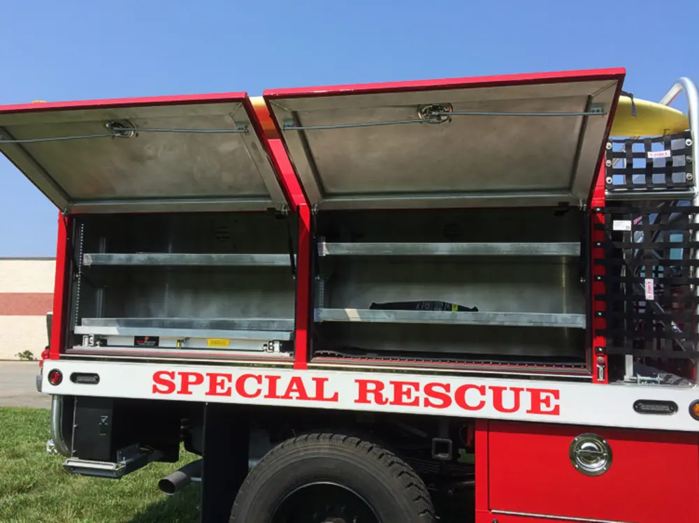 Exterior view of small fire truck showing cab, body compartments, and wheel/tire area.