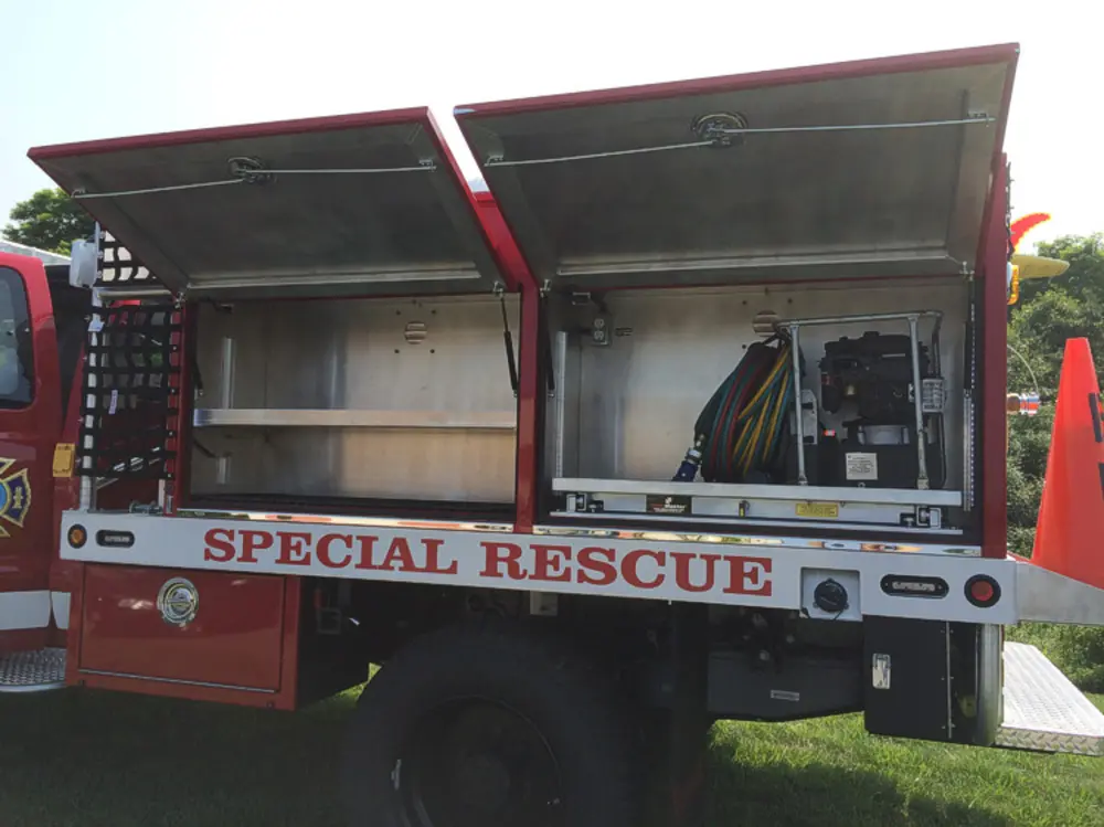 Exterior view of small fire truck showing cab, body compartments, and wheel/tire area.