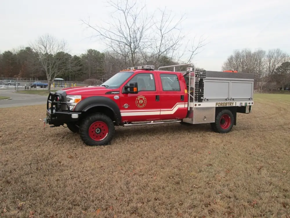Exterior view of small fire truck showing cab, body compartments, and wheel/tire area.