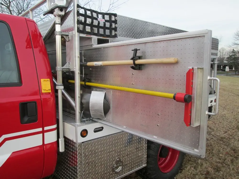 Exterior view of small fire truck showing cab, body compartments, and wheel/tire area.