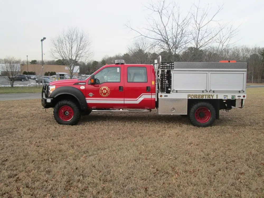 Exterior view of small fire truck showing cab, body compartments, and wheel/tire area.