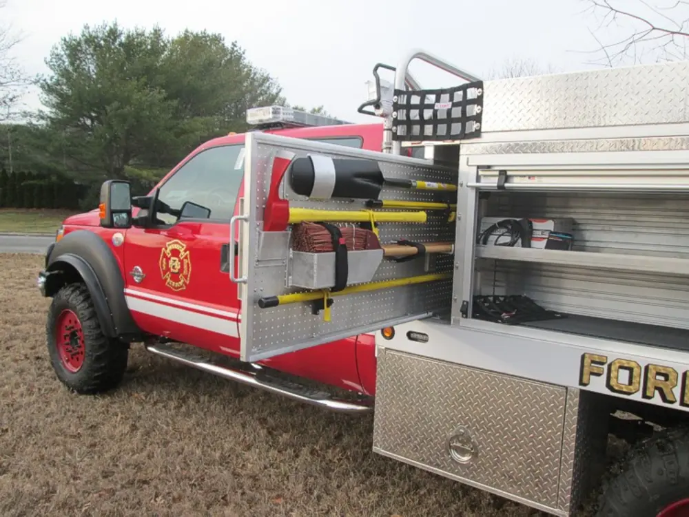 Exterior view of small fire truck showing cab, body compartments, and wheel/tire area.