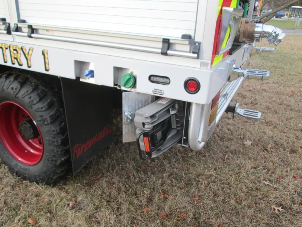 Exterior view of small fire truck showing cab, body compartments, and wheel/tire area.
